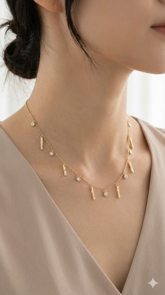 Close-up of a woman wearing a delicate gold chain necklace featuring alternating charms of textured vertical bars and small round clear crystals.
